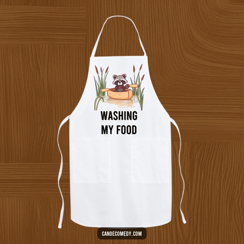 Funny raccoon apron showing a raccoon navigating a canoe through reeds, perfect for adding wit and fun to cooking.